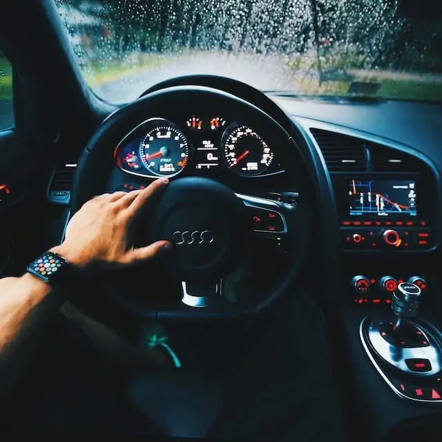 A driver's hand on the steering wheel of a performance car on a wet road