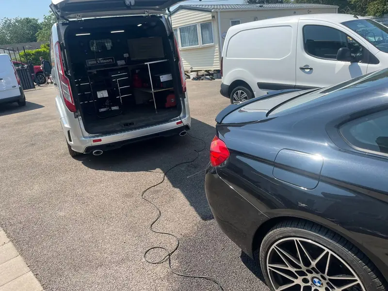 The van parked behind a BMW with its cable running to the car